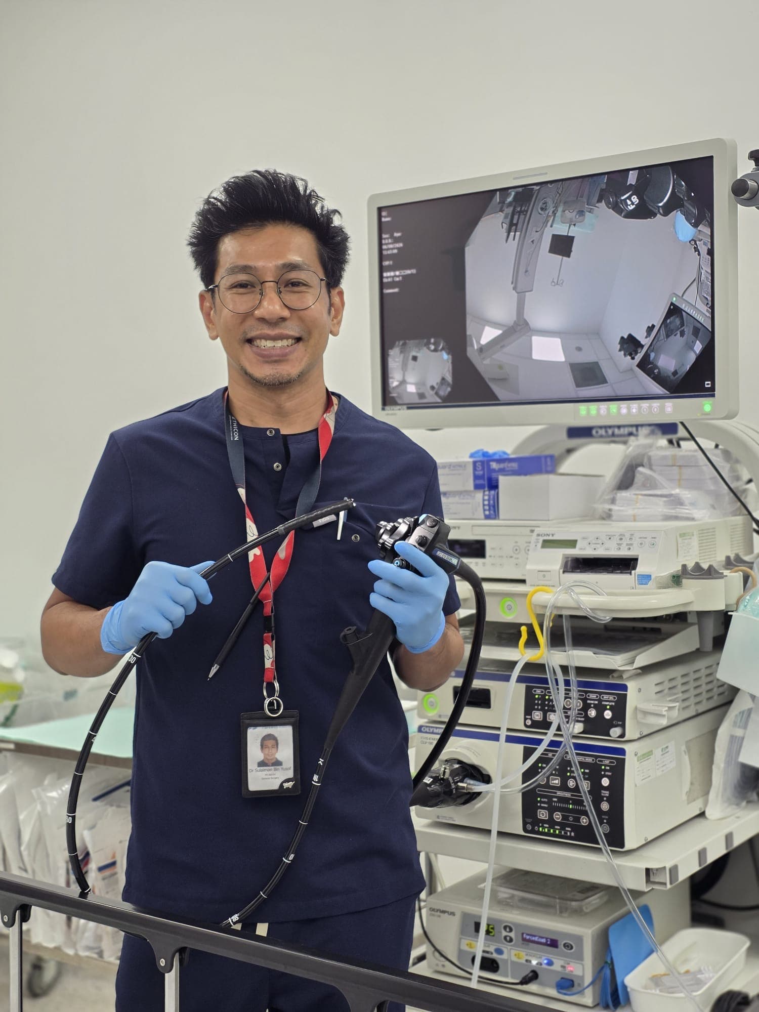 Dr Sulaiman Bin Yusof holding endoscopy equipment beside an Olympus endoscopy stack.