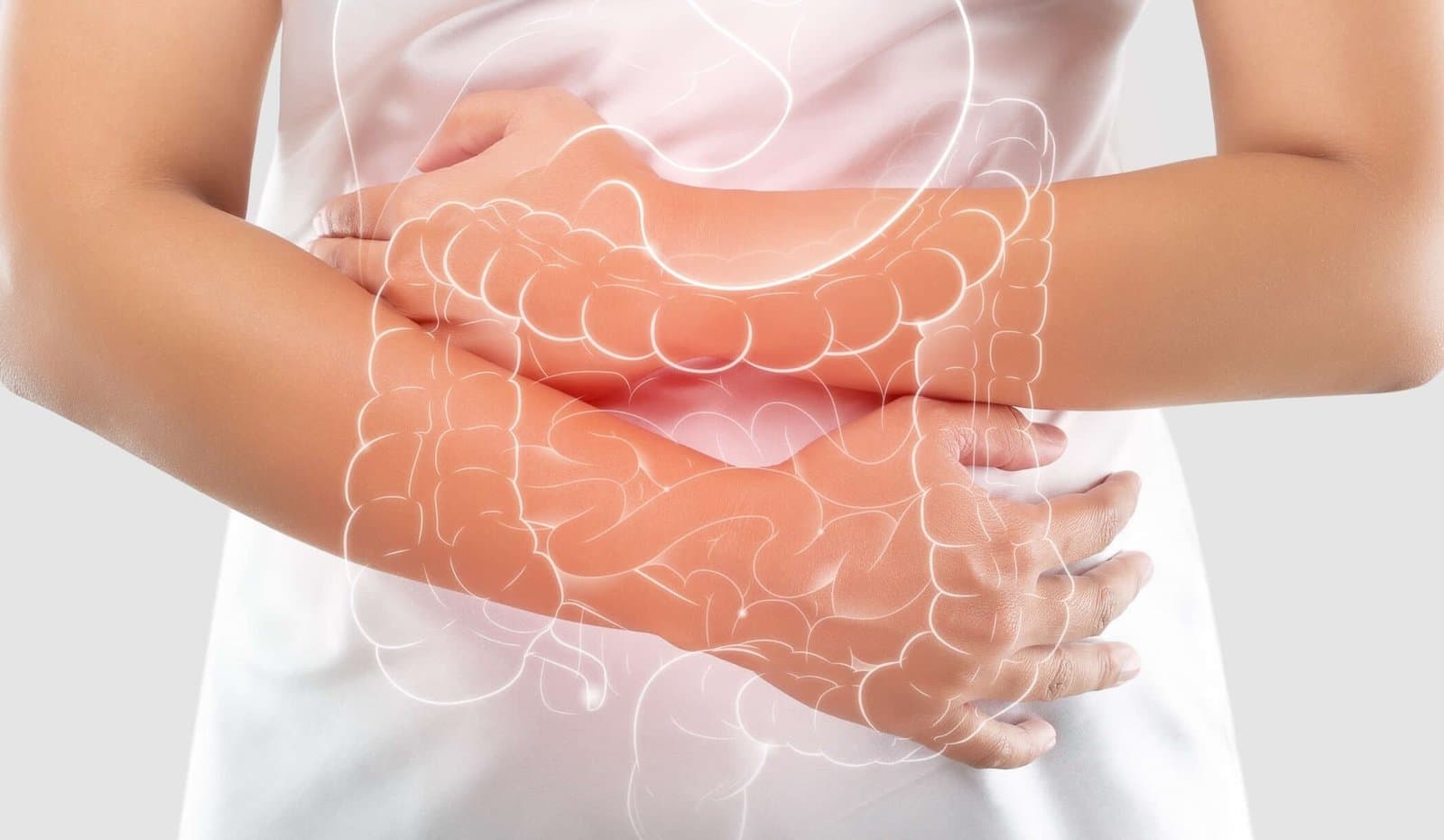 A person photographed from the chest down in a white top, both hands clasped over the lower abdomen. The large bowel is drawn as a translucent overlay across the abdomen, its lower loops lit pink.