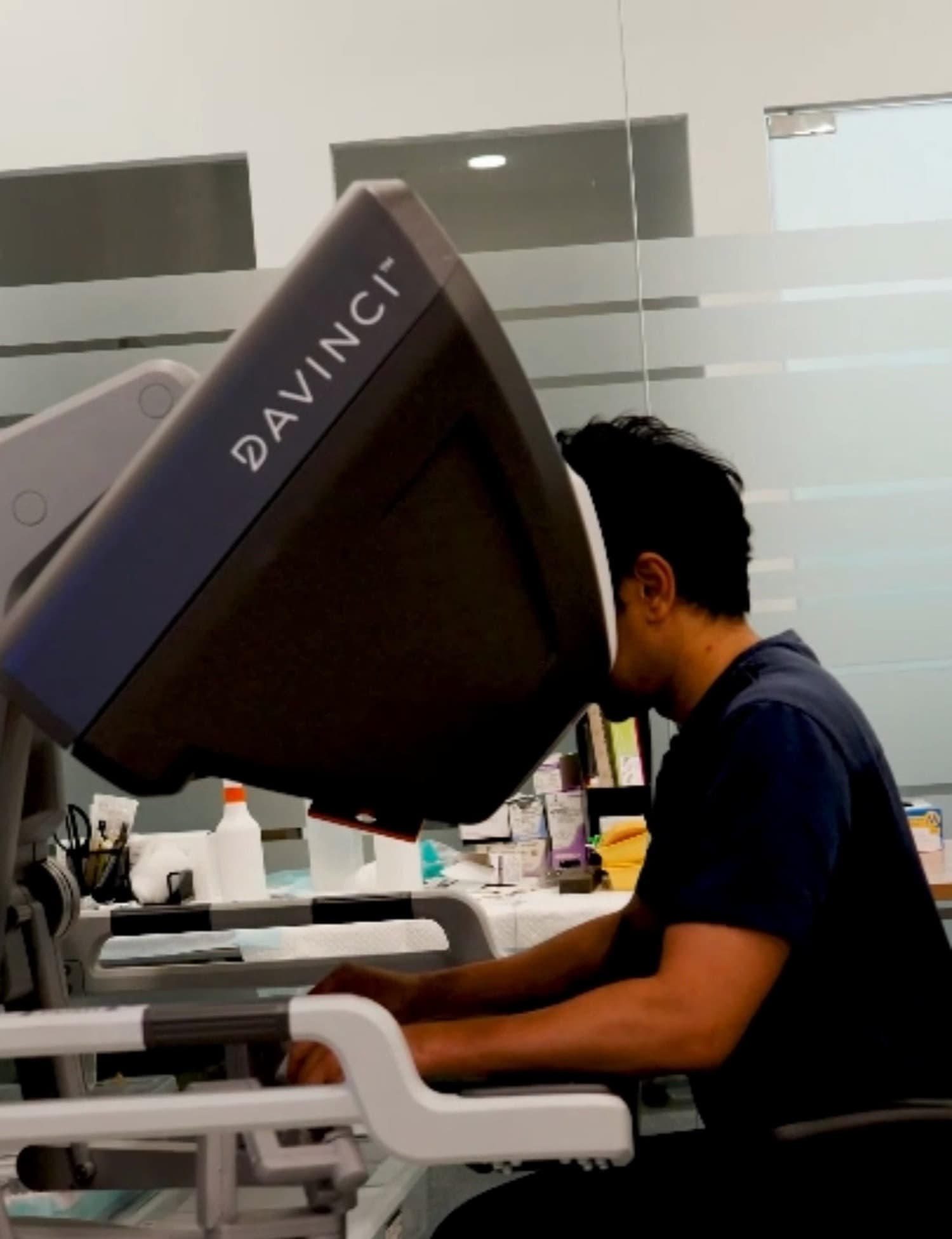 Dr Sulaiman Bin Yusof seated at a da Vinci surgeon console in an operating theatre, leaning into the binocular viewer with his hands at the controls.